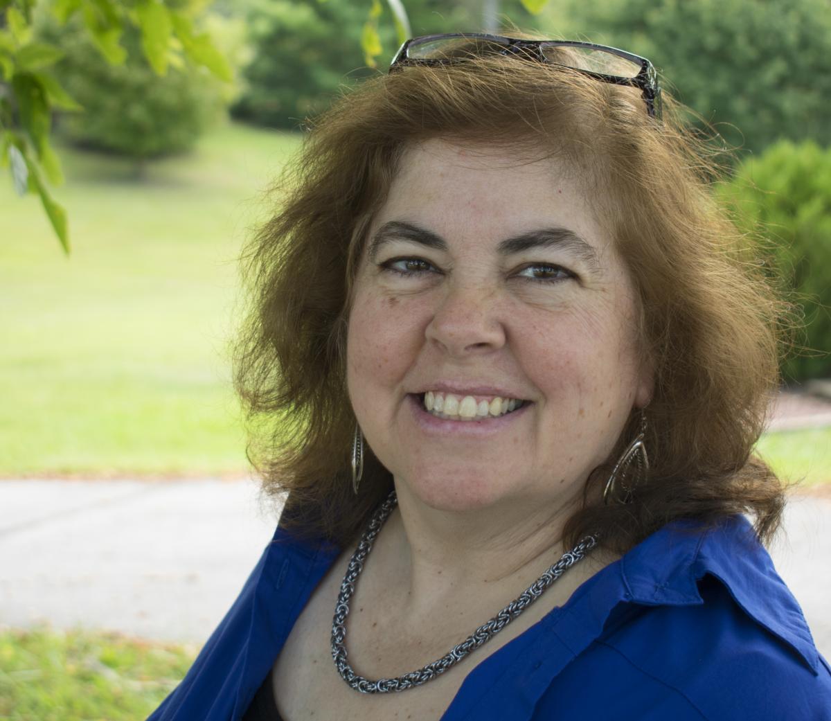 Image of woman with reddish shoulder length hair wearing a blue blouse.