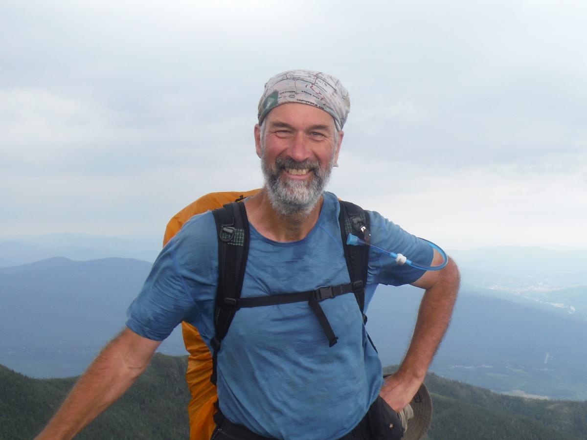Ed Riggs standing with a backpack on and mountains in the background.