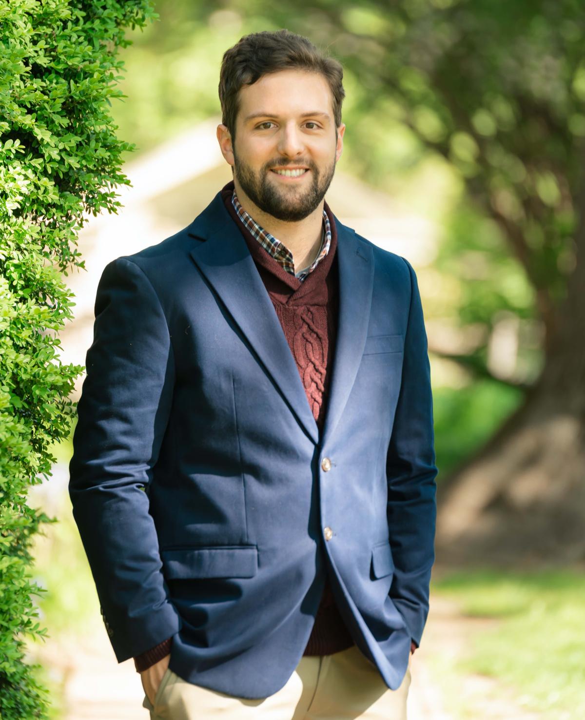 Image of a man with brown hair, brown beard, and a blue sportscoat. 